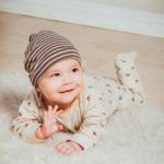 Baby on floor with hat on, smiling