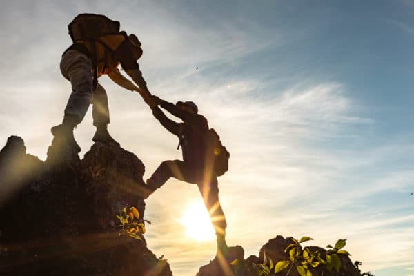 One person helping another person climb up a rock in the wilderness